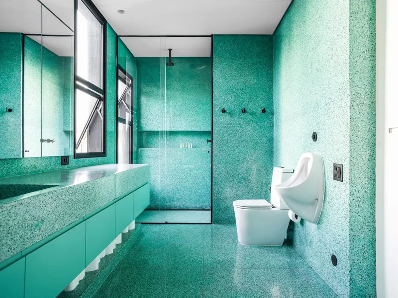 Bathroom clad in turquoise terrazzo tiles with integrated vanity and glass-enclosed shower