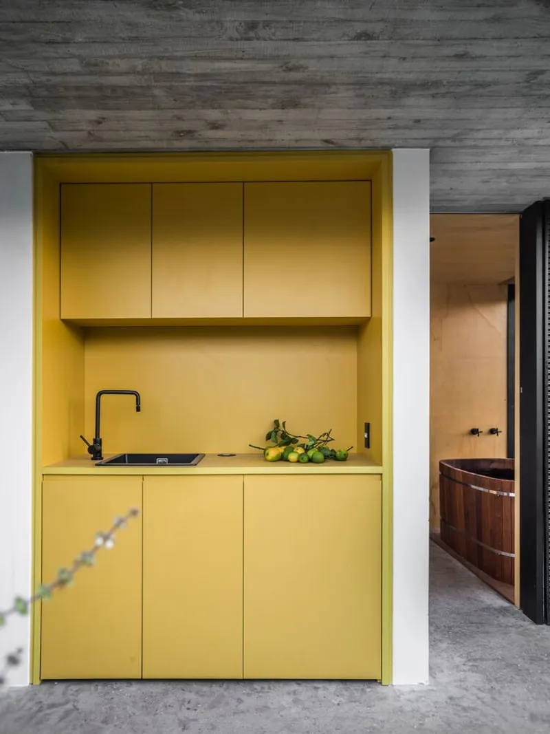 Yellow kitchenette alcove with flush cabinetry beneath board-formed concrete ceiling and polished concrete floor