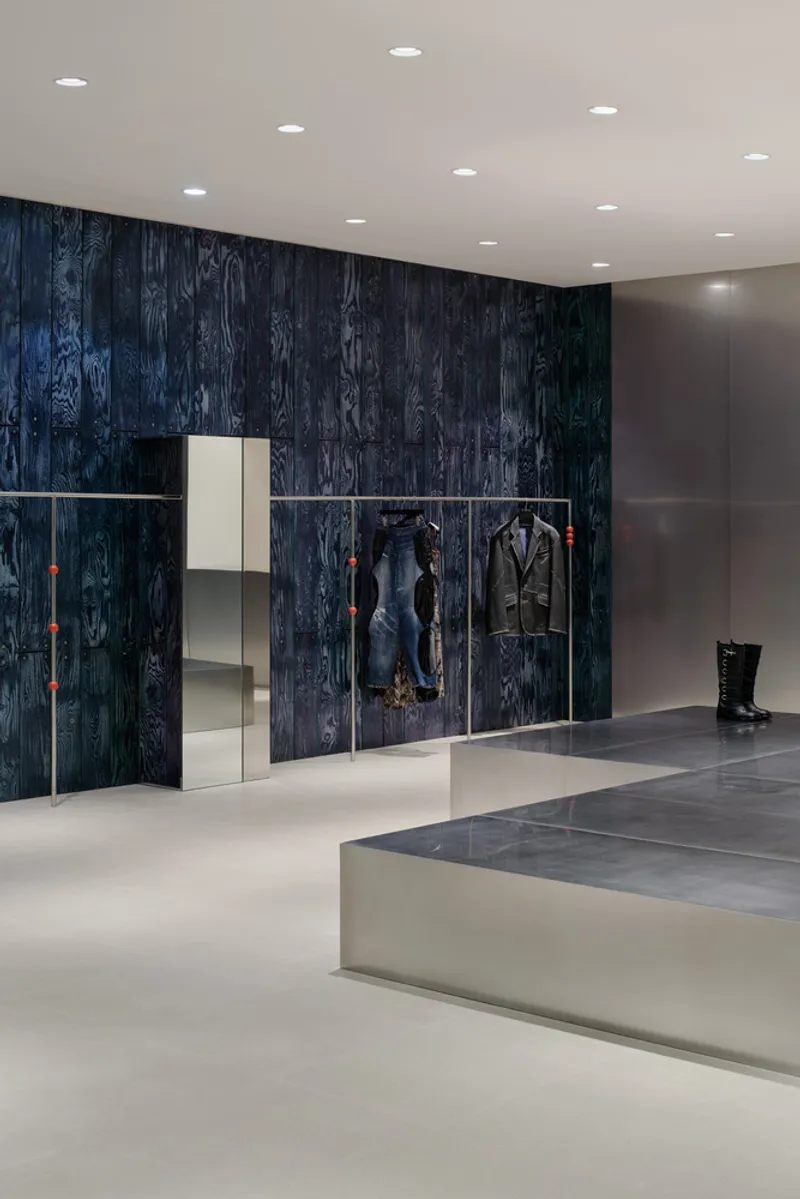 Charred wood feature wall with integrated display shelving and chrome rails against white resin flooring