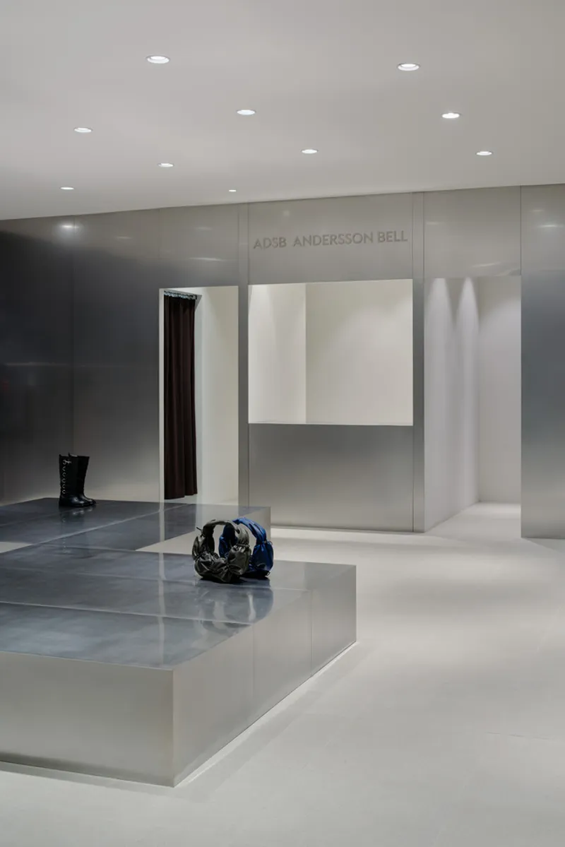 Retail interior with layered glass partitions, white display platforms and a dark accessory on polished stone