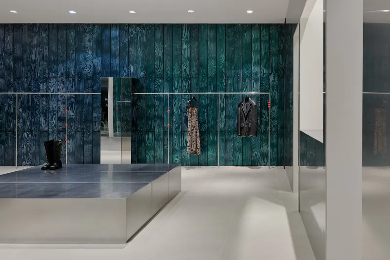 Blue-tinted charred wood wall with horizontal metal display rails holding garments above a white platform