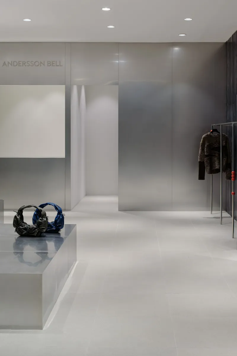 White display platform with a sculptural handbag beside a translucent glass partition and recessed downlights