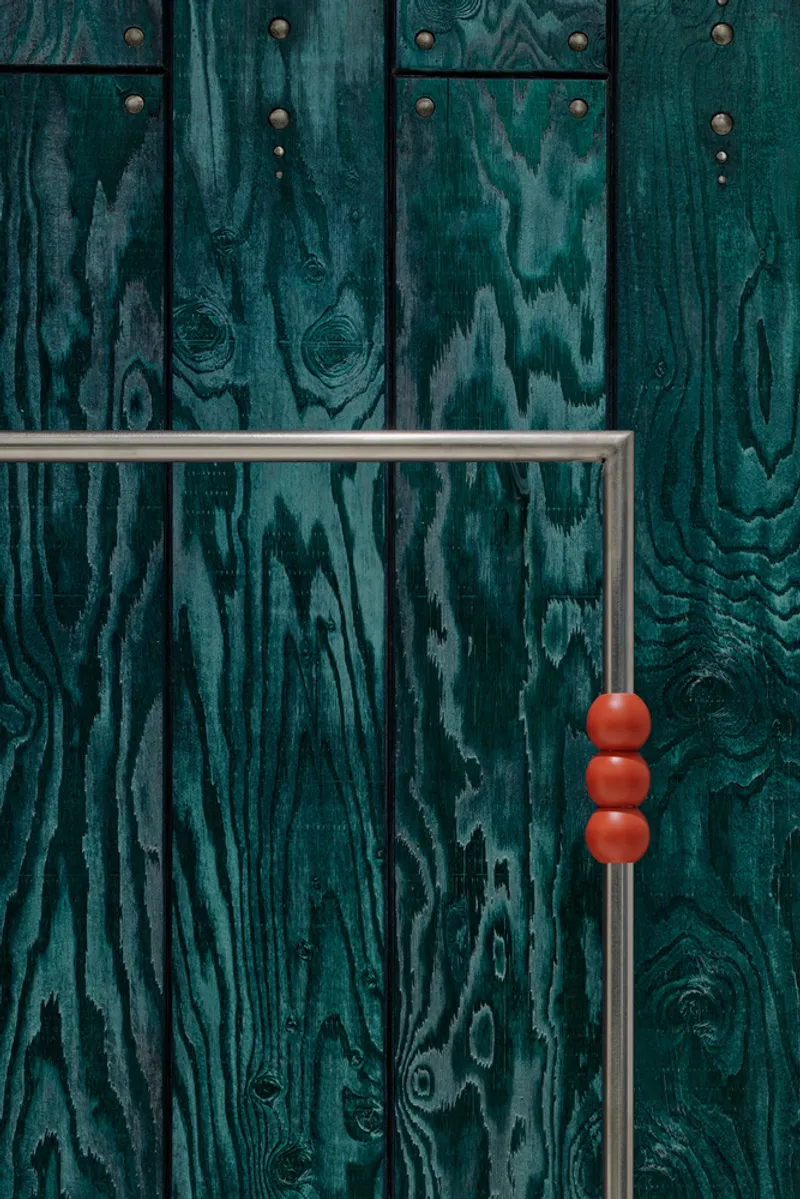 Detail of chrome hanging rail with orange spherical knobs against teal woodgrain wall panels