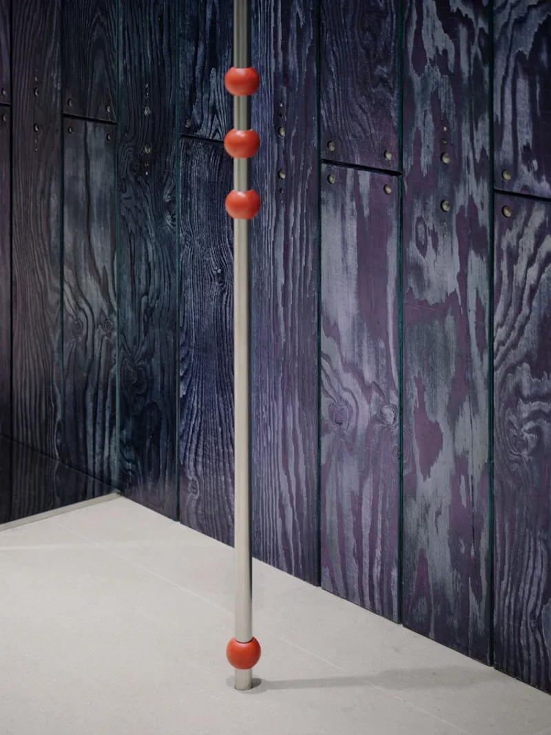 Floor-to-ceiling chrome pole with orange spherical accents beside dark stained wood panel wall
