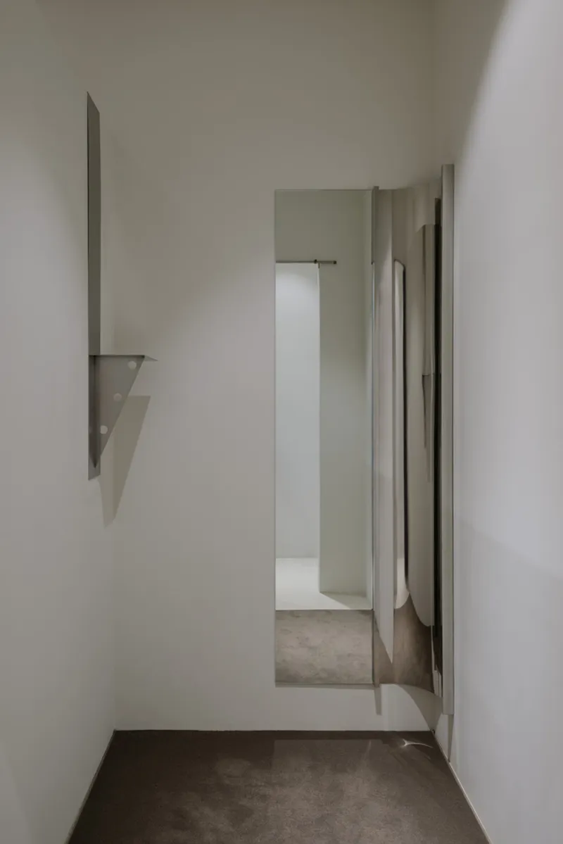 Narrow corridor with white walls and grey concrete floor leading to a bright opening ahead