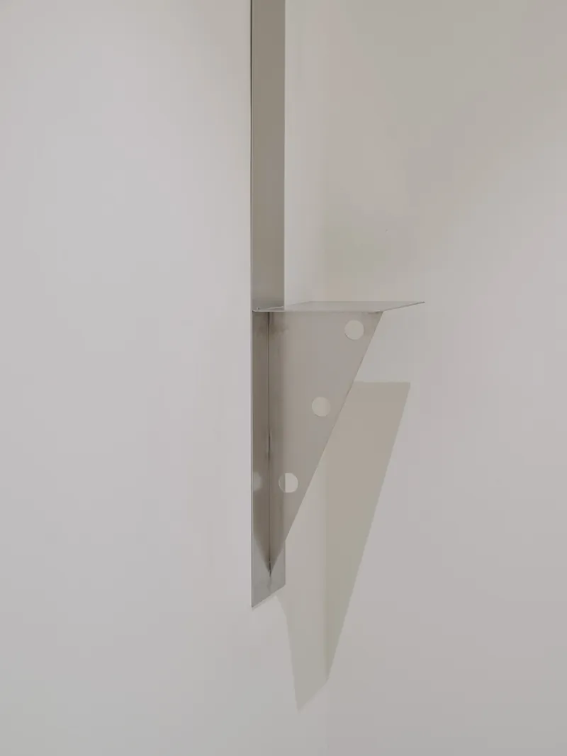 Detail of a folded metal bracket with bolt holes protruding from a white wall corner