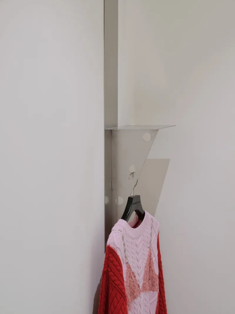Metal wall bracket with pink and red knitted garment hanging from a brass hook
