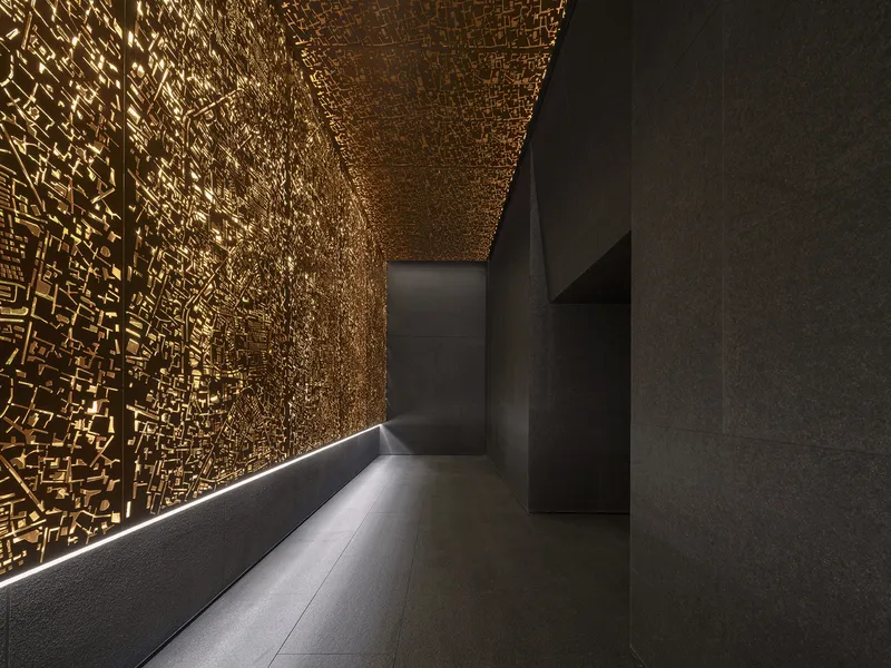 Corridor with perforated golden ceiling and cove lighting along the base of textured dark walls