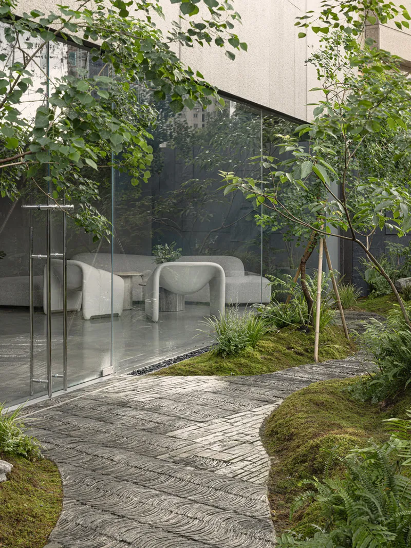 Interior courtyard with curved stone paving, planted beds of moss and ferns framed by glazed walls