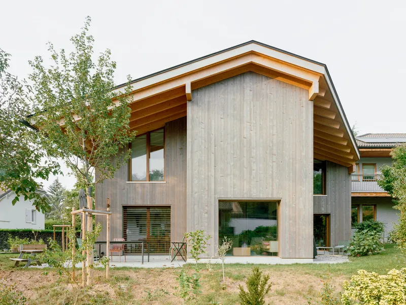 Vertical wood cladding facade with exposed timber eaves and young trees in the front garden