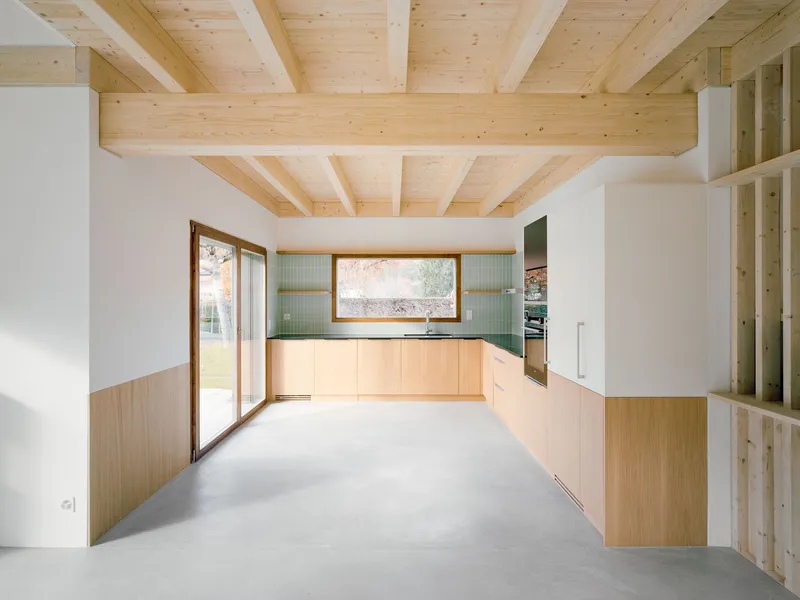 Kitchen with light wood cabinetry, green tile backsplash and exposed beam ceiling with polished concrete floor