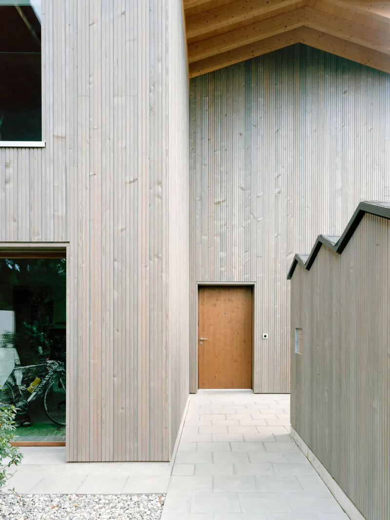 Exterior entry path with pale stone pavers leading to a timber door set in vertical wood cladding