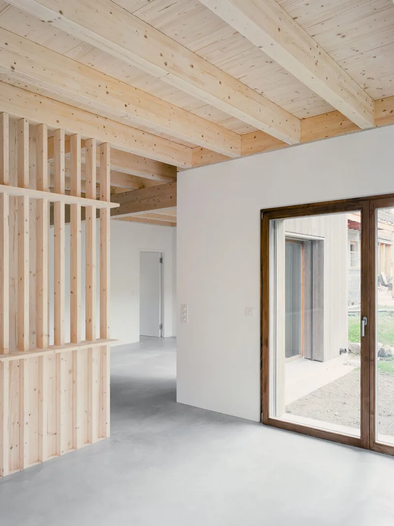 Open living space with vertical timber slat partition and glass door framing view to garden