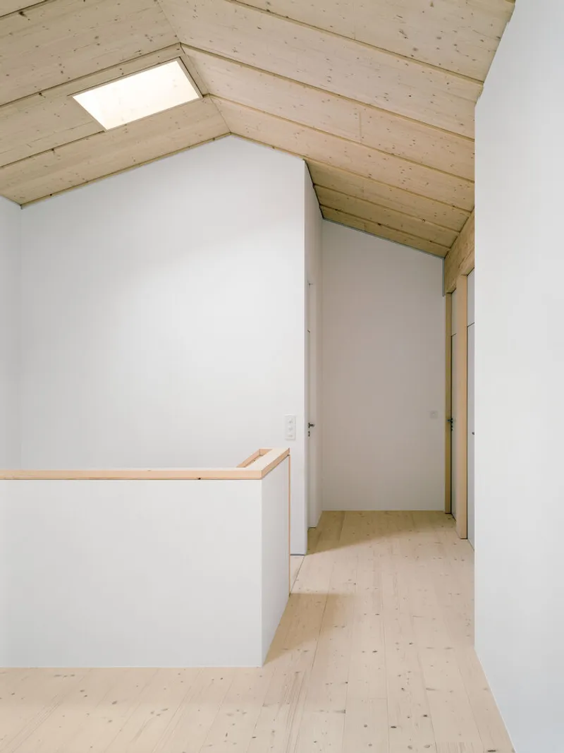 Sloped ceiling hallway with plywood flooring and skylight illuminating the corridor to a door