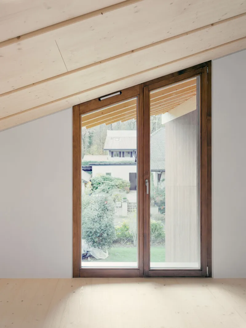 Interior view of a timber-framed window with vertical wood ceiling beams overlooking a garden