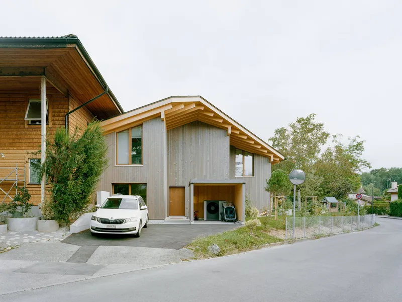 Street view of a gabled timber house with exposed rafters and a parked car