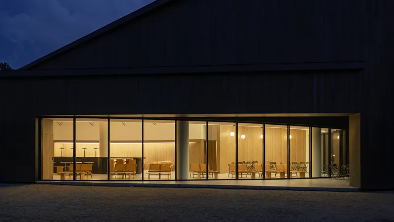 Floor-to-ceiling glass wall with timber-framed bays illuminated at dusk under a dark timber gable