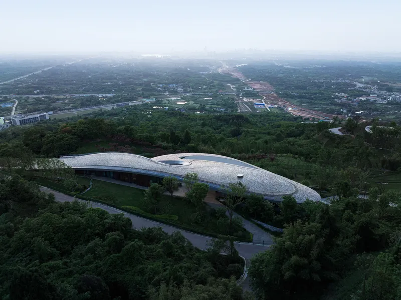 Aerial view of the undulating white roof nestled in dense green foliage at dusk