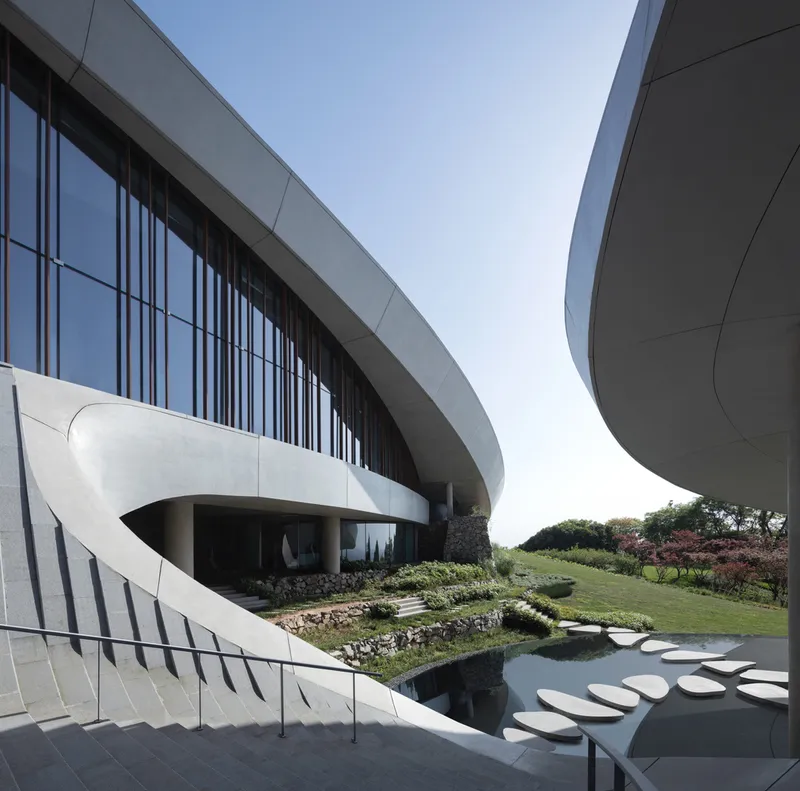 Curved concrete terrace with reflective pool and stepping stones leading to vertical timber screens