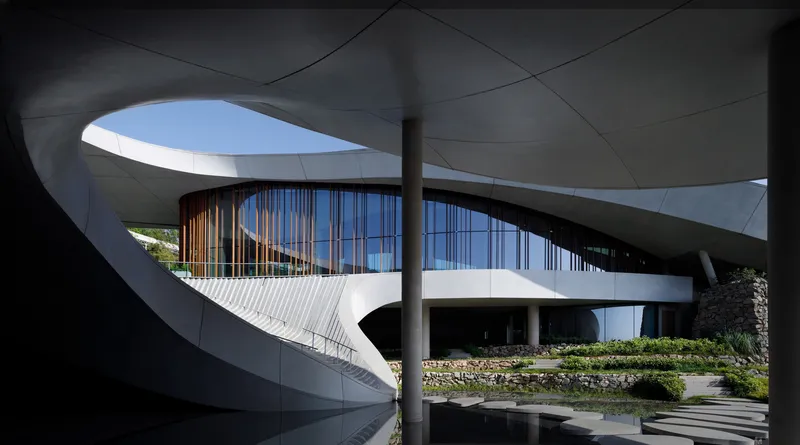 View through curved concrete canopy framing the timber screen facade and stone steps beyond