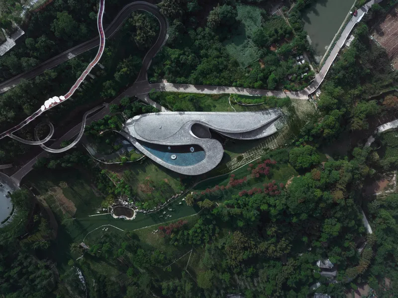 Drone view of the biomorphic roof with central pool nestled among winding roads and vegetation
