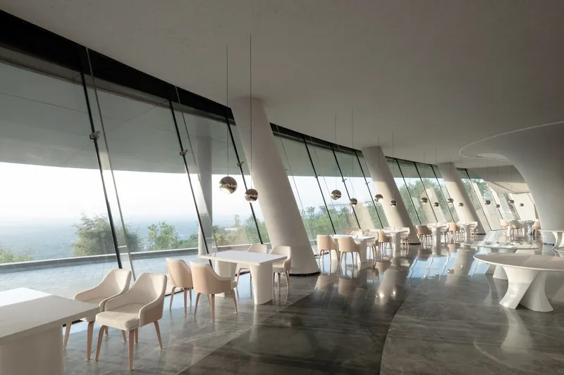 Dining area with angled glass wall sections and pendant lights suspended over white circular tables