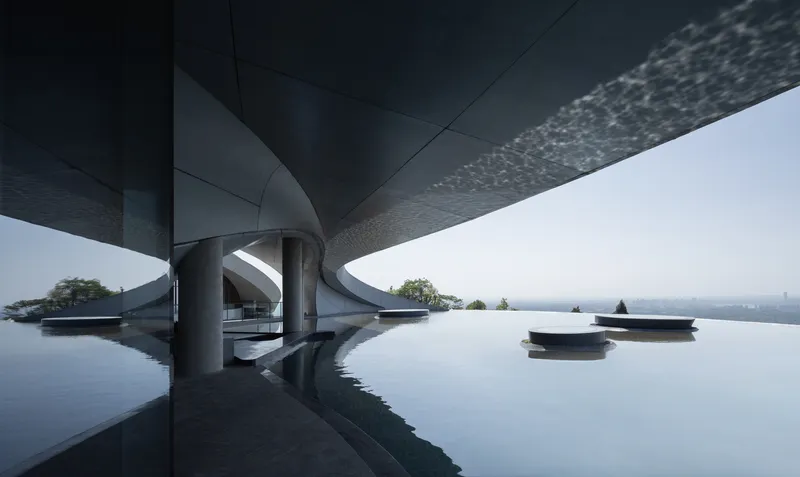 Infinity pool beneath cantilevered roof with cylindrical columns and textured soffit panels in morning haze