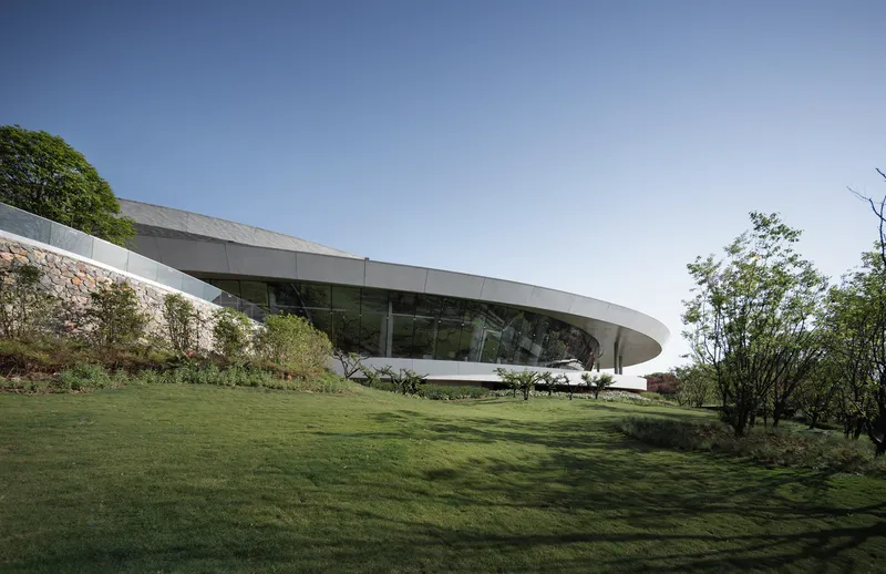 Exterior view of the sweeping roof canopy hovering above glazed perimeter on a grassy hillside