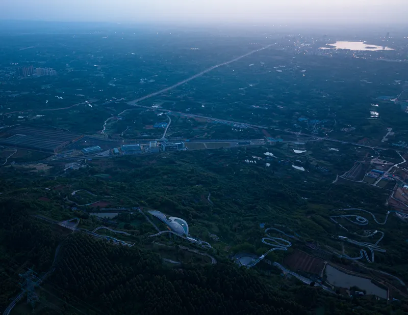 Drone view of curved roof volumes embedded in forested valley at dusk