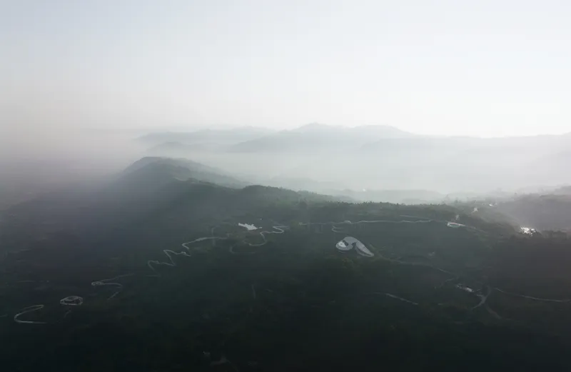 Aerial view of curved roofs nestled among forested hillsides in morning mist