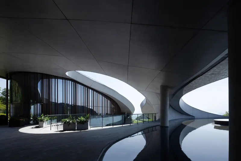 Covered terrace with reflecting pool framing the curved vertical louver facade and cantilevered roof