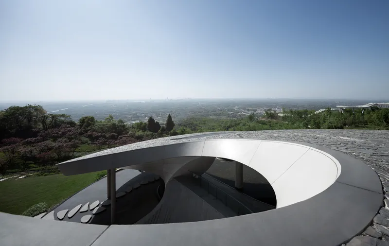 Rooftop oculus with smooth concrete edges framing the gallery entrance and landscape beyond