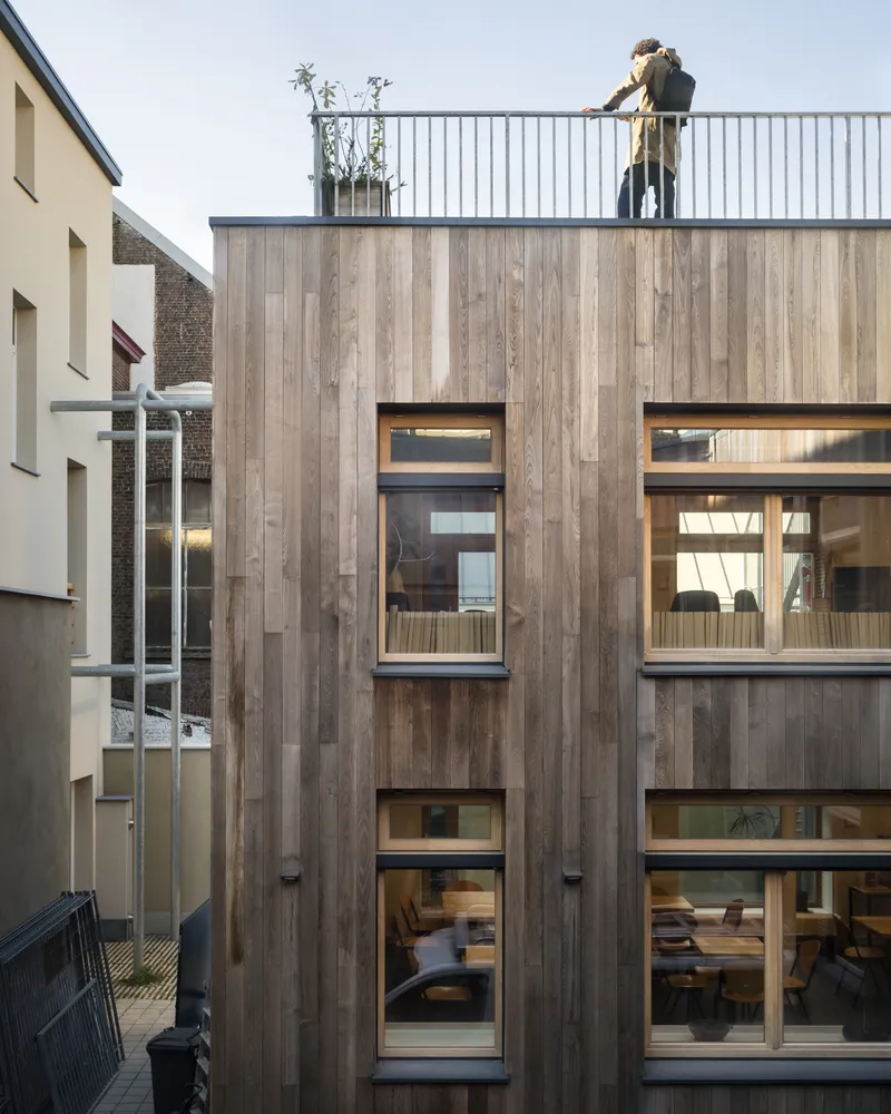 Rear elevation showing the timber-clad volume with stacked horizontal windows and a figure on the rooftop deck