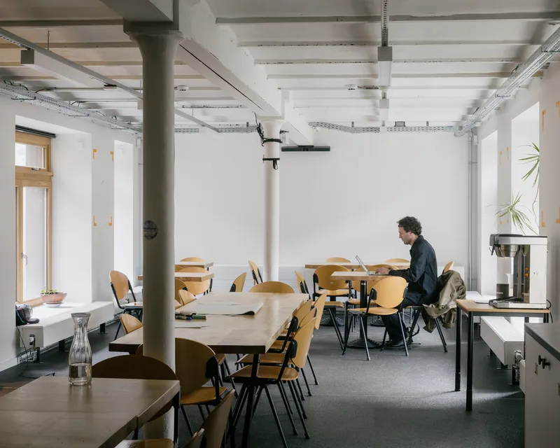 Open workspace with exposed ceiling beams, painted steel columns, and a person seated at a table