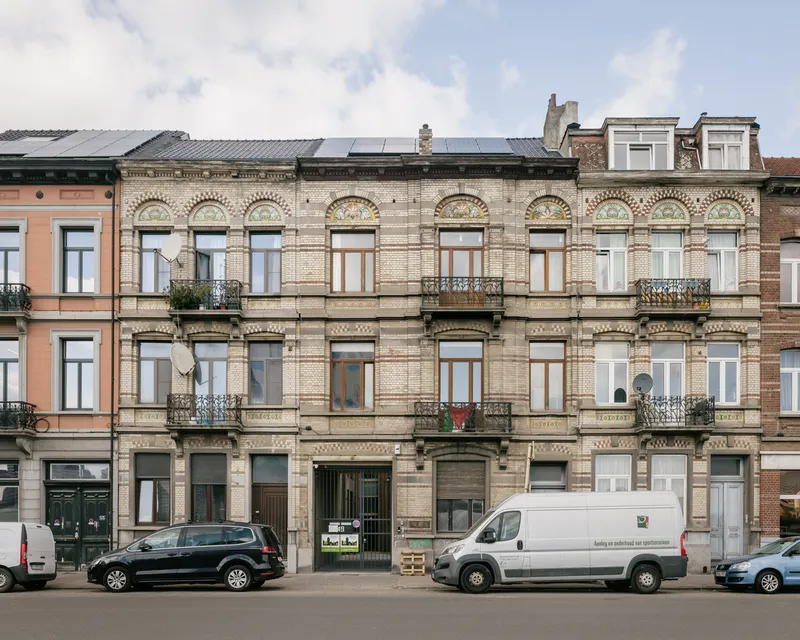 Street facade of a cream brick townhouse with arched windows and solar panels on the roofline