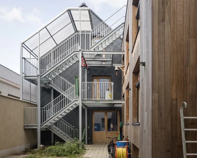Galvanized steel stair connecting multiple levels in a narrow courtyard flanked by timber cladding