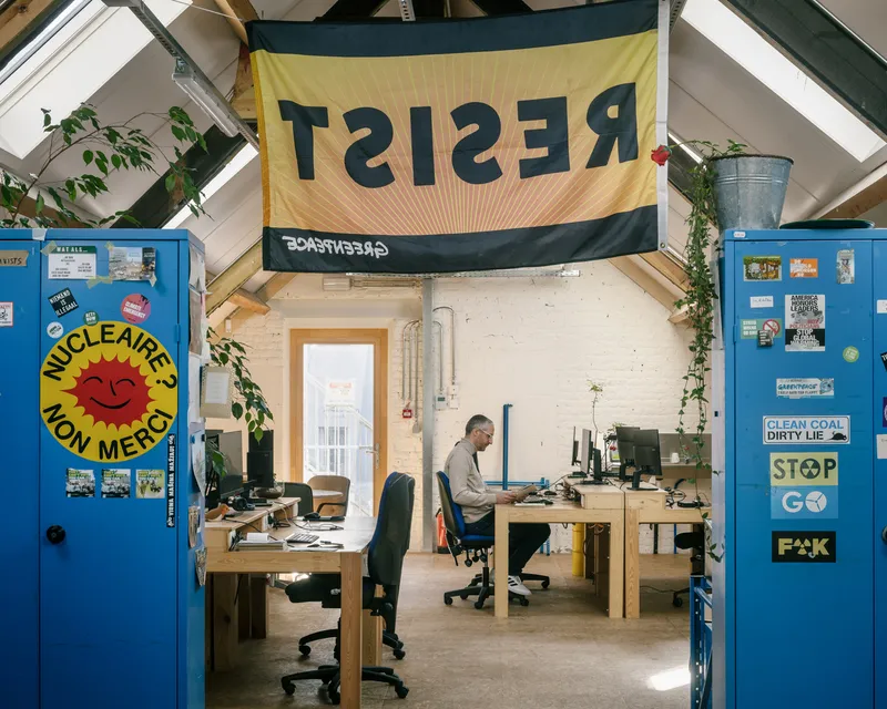 Office workspace with exposed timber rafters, painted white brick walls, and blue doors with protest stickers