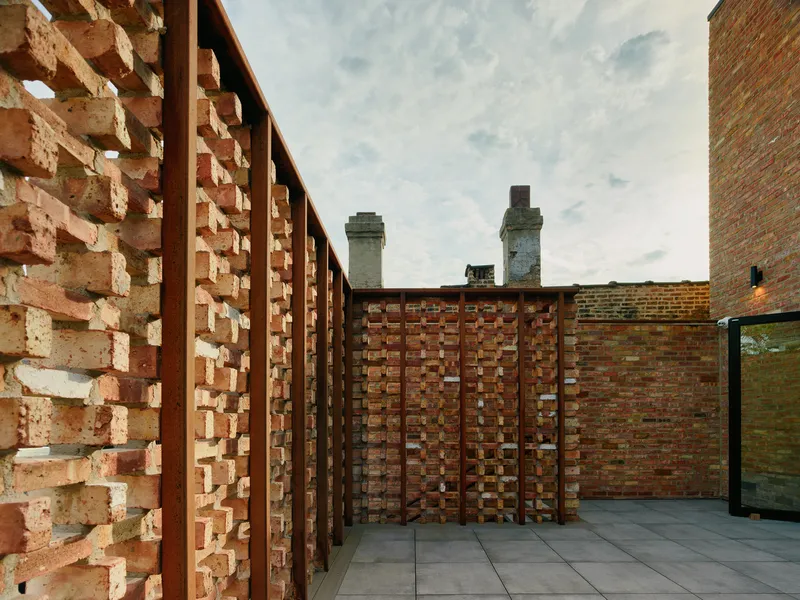 Rooftop terrace with perforated brick screens and steel frames beneath a cloudy sky