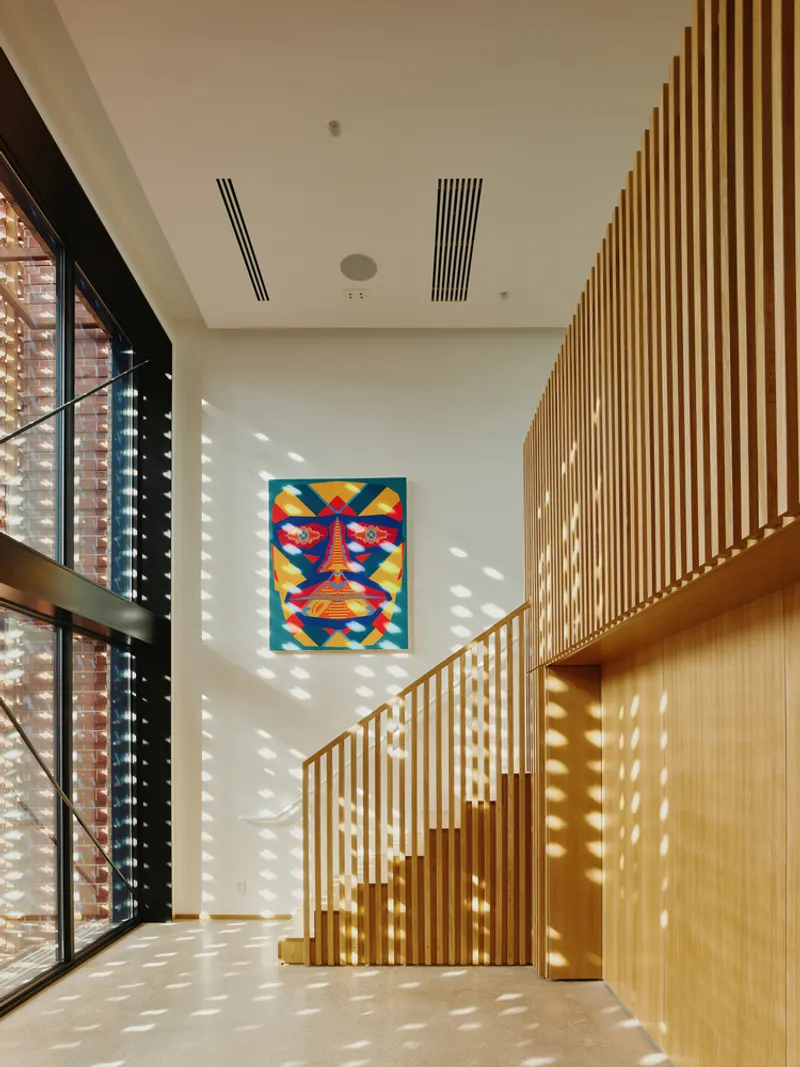Timber slat staircase and balustrade with dappled sunlight filtering through perforated brick facade