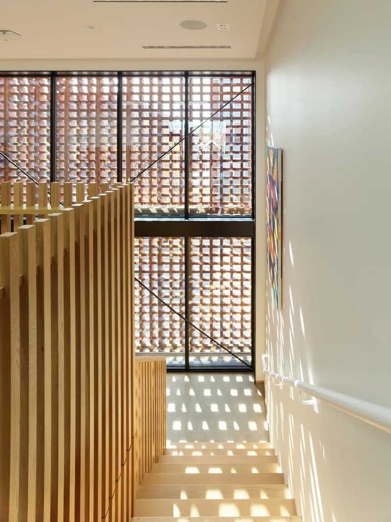Timber staircase descending toward perforated brick screen wall with patterned shadow