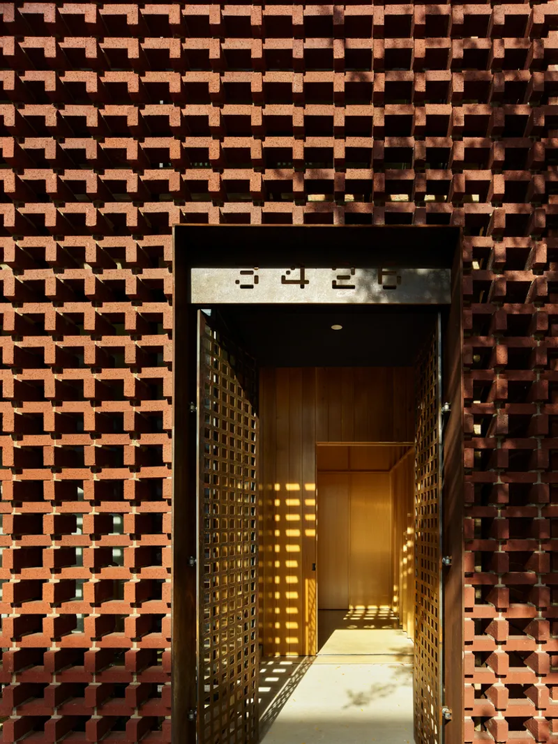 Entry passage through perforated brick wall showing illuminated corridor with house numbers above