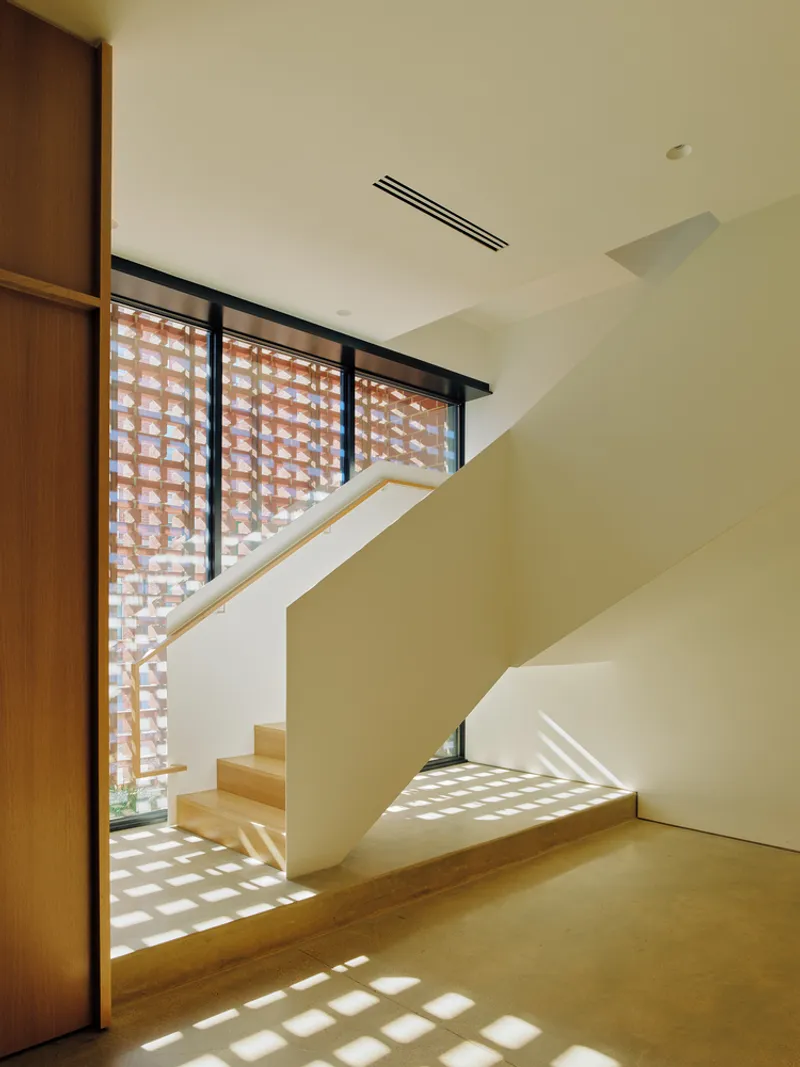 Interior staircase with timber treads and perforated brick screen filtering light into stairwell