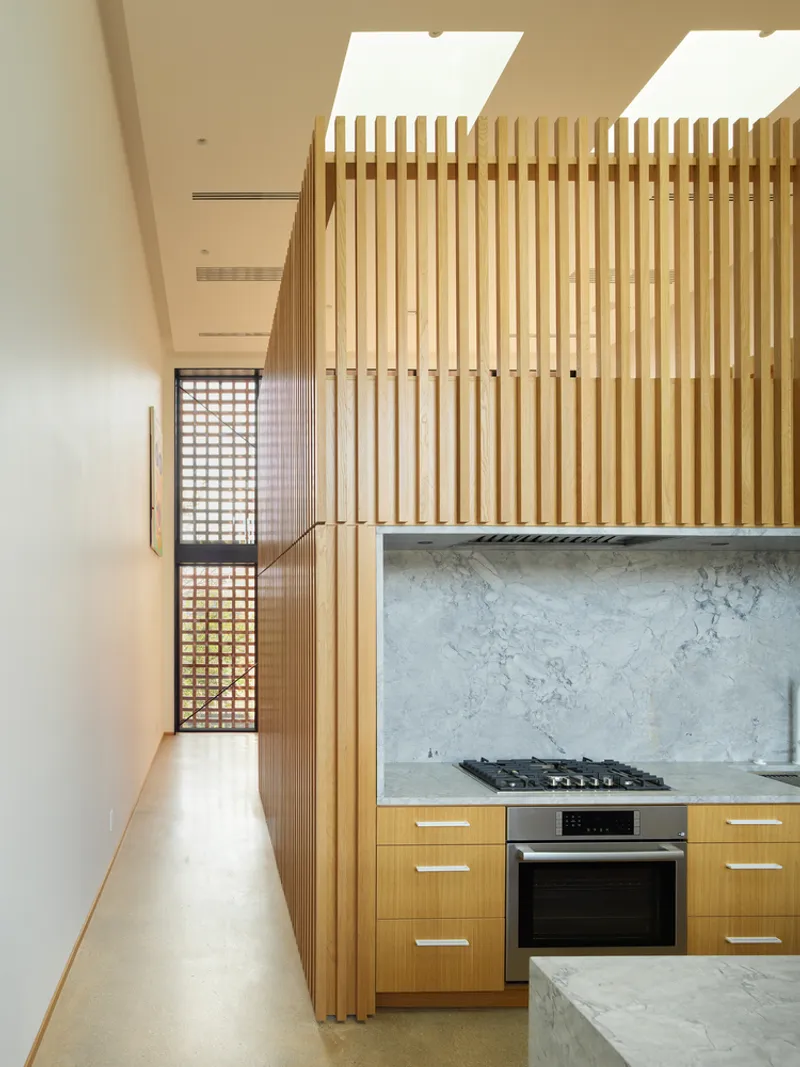 Kitchen with vertical wood slat screen and marble countertop beneath clerestory skylights