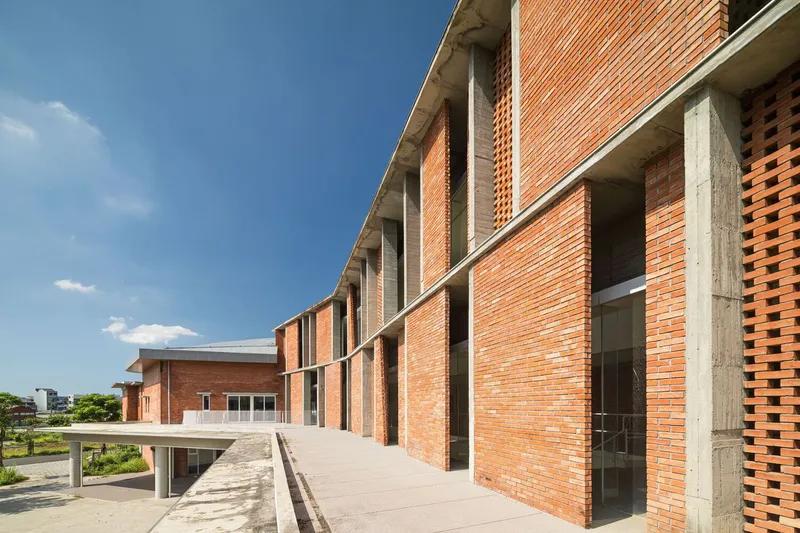 Upper level walkway with red brick facade punctuated by vertical window openings and concrete columns under blue sky