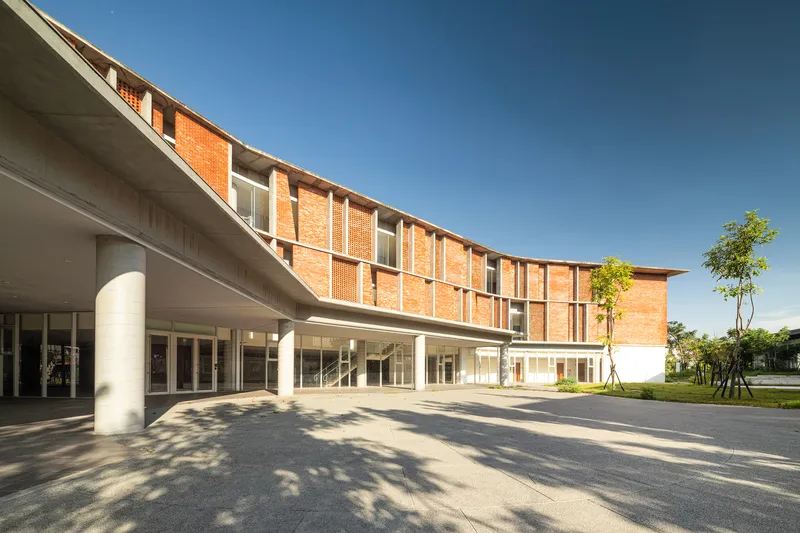 Covered entry drive with cylindrical concrete columns and curved brick facade casting shadows on the paved plaza