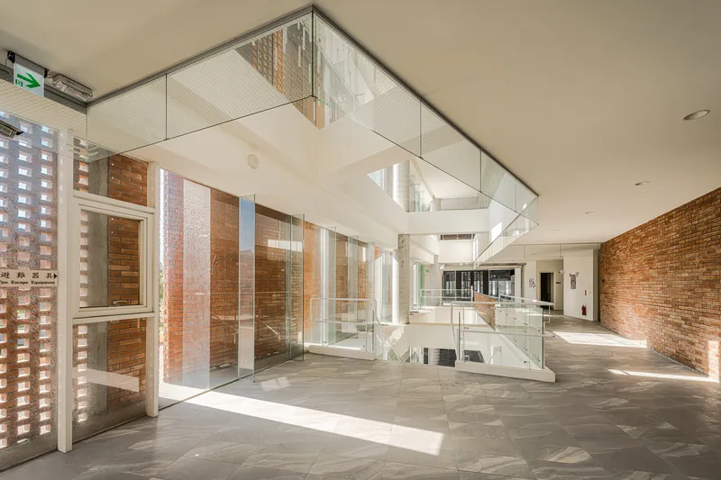 Interior atrium with glass-enclosed stairwell, brick walls, and stone floor lit by afternoon sunlight