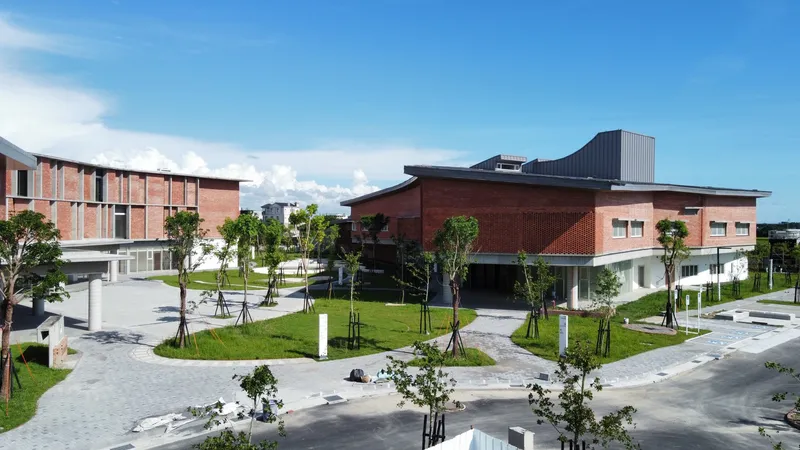 Campus courtyard with planted lawn and paved pathways between brick-clad buildings under a clear blue sky