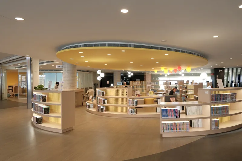 Library circulation desk with curved plywood shelving beneath a circular yellow ceiling soffit