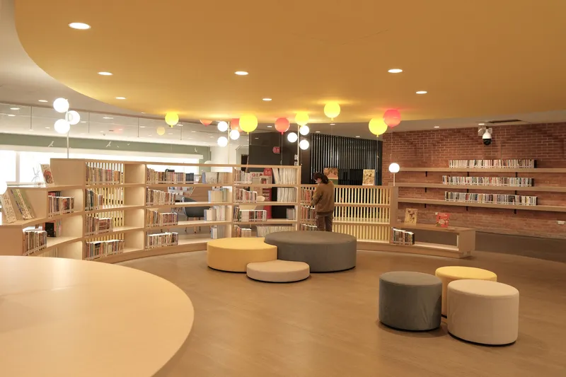 Reading area with circular upholstered seating beneath a yellow ceiling and colorful balloon pendant lights