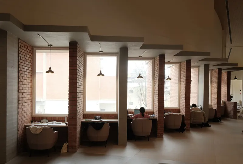 Reading alcoves with brown leather armchairs between red brick columns and tall windows overlooking bare trees